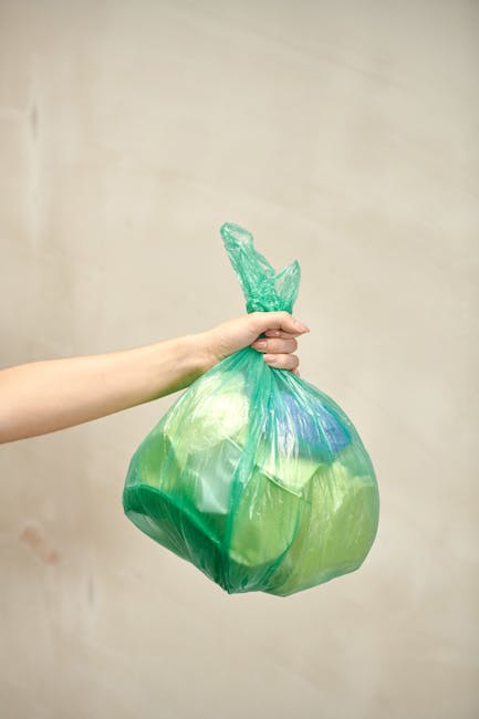 A large collection of mixed household and commercial waste is piled on a paved urban sidewalk in front of a commercial building, with some rubbish spilling onto the street. The waste includes crumpled